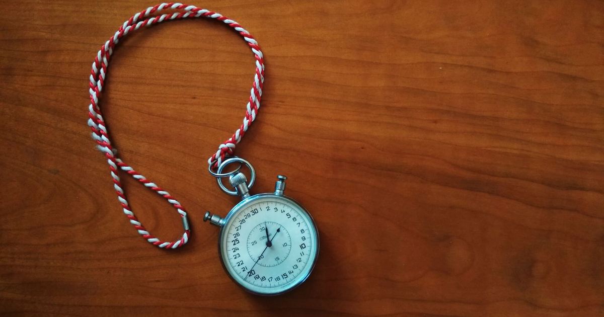 An antique silver stopwatch lying on a warm wooden table, its cord looped beside it.